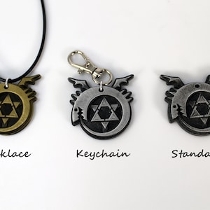 May include: Three versions of a metal pendant featuring a black and silver design of a circle with a star inside and a dragon head on the side. The pendant is available as a necklace, keychain, and standard.