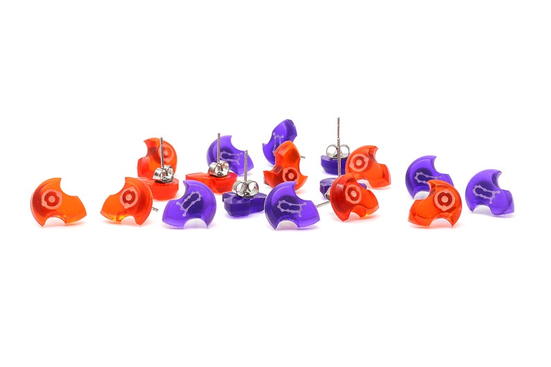 May include: A set of 10 earrings, 5 are orange and 5 are purple. Each earring is shaped like a crescent moon with a small white design in the center. The earrings have silver posts.