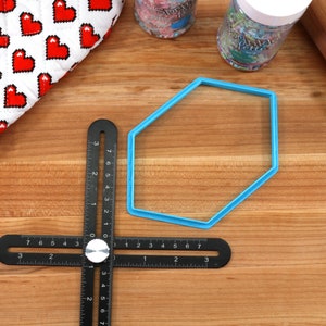 Op de afbeelding: Een blauwe plastic zeshoekige koekjesvormer op een houten oppervlak met een zwarte liniaal en een deegroller.