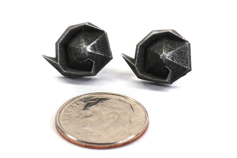 May include: A pair of silver geometric earrings, each shaped like a spiral, shown next to a US dime for scale.