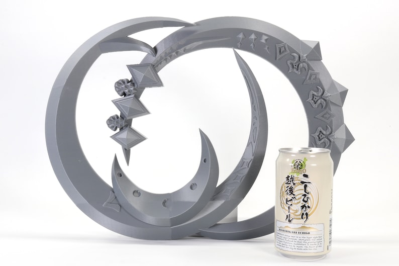 May include: A gray 3D printed sculpture of two interlocking crescent moons with intricate designs. The sculpture is about the size of a standard can of beer.