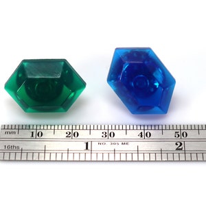 May include: Two plastic gems, one green and one blue, are shown next to a ruler. The green gem is about 1 inch wide and the blue gem is about 1.5 inches wide.