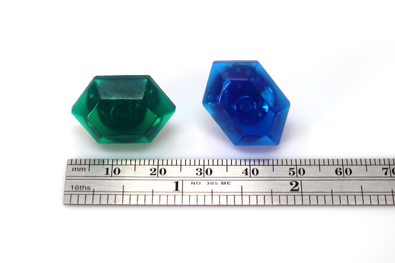May include: Two plastic gems, one green and one blue, are shown next to a ruler. The green gem is about 1 inch wide and the blue gem is about 1.5 inches wide.