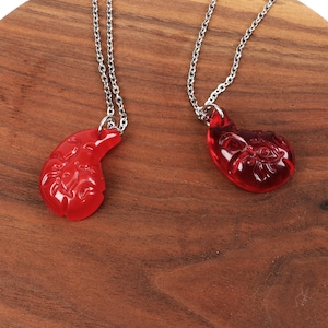 May include: Two red glass pendant necklaces with silver chains. The pendants are shaped like a teardrop and have intricate designs.