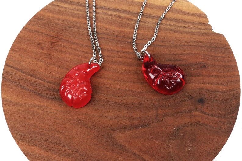 May include: Two red glass pendant necklaces with silver chains. The pendants are shaped like a teardrop and have intricate designs.