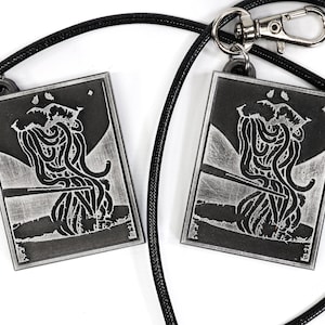 May include: Two silver-toned pendants with black and white images of a creature with tentacles hanging from a black cord with a silver clasp.
