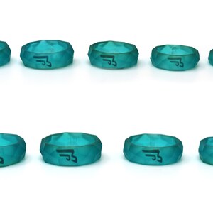 May include: Eight teal blue silicone rings with a black symbol on each. The rings are different sizes and have a faceted design.