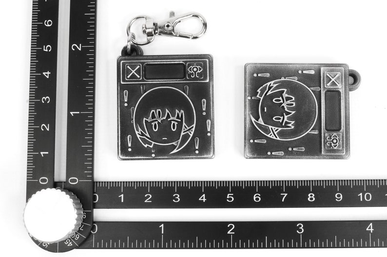 May include: Two silver metal keychains with a cartoon character design. The keychain on the left has a silver metal ring and a silver metal clasp. The keychain on the right has a silver metal clasp. Both keychains have a black and white cartoon character design with the text "X" and "SP" on the keychains.