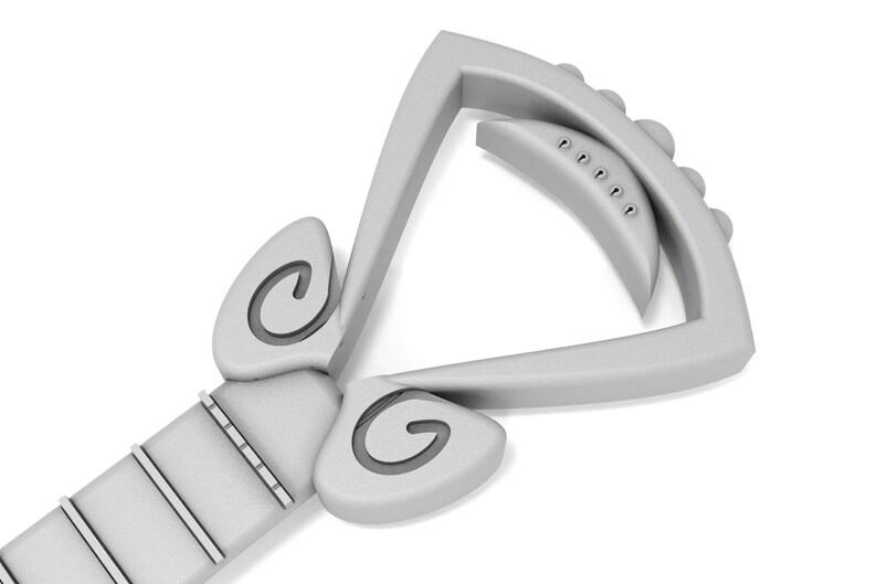 May include: A silver guitar capo with a unique design featuring two curved, spiral-shaped accents on either side of the capo. The capo has a series of small, round knobs on the top.