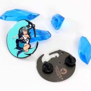 May include: A blue and black enamel pin featuring a cartoon woman with blue hair holding a pickaxe, standing on a crescent moon. The back of the pin is black with the text "Loot Cave Co." and a logo.