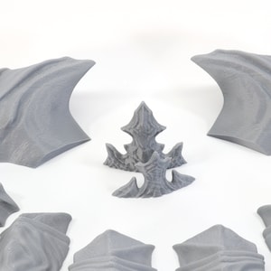Pode incluir: Um conjunto de asas e espinhas de drag&atilde;o impressas em 3D na cor cinza. As asas s&atilde;o curvas e t&ecirc;m uma superf&iacute;cie texturizada. As espinhas s&atilde;o pontiagudas e t&ecirc;m uma borda dentada.