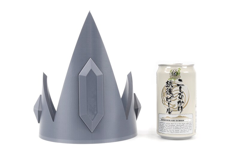 May include: A gray 3D printed crown with a pointed top and crystal-like details. The crown is next to a can of Japanese beer.