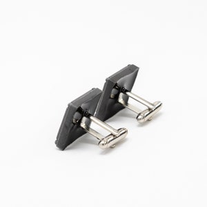 May include: A pair of gray square cufflinks with silver metal clasps.