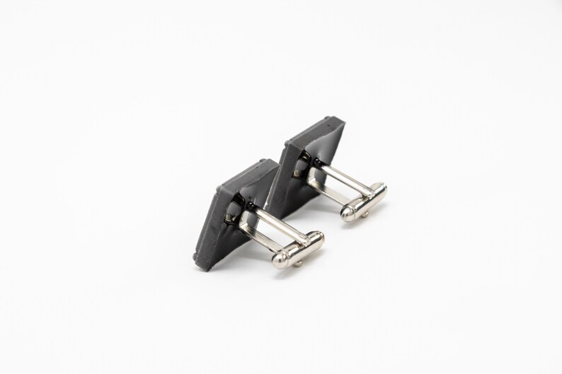 May include: A pair of gray square cufflinks with silver metal clasps.