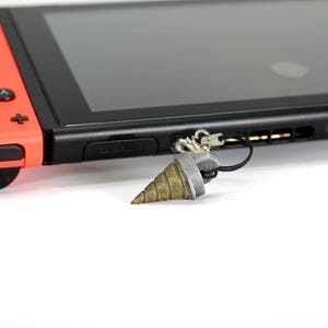May include: A red and black Nintendo Switch console with a grey drill bit keychain attached to the console's strap.