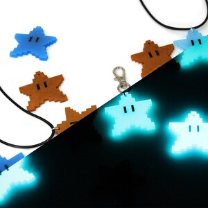 May include: A set of glow-in-the-dark star-shaped pendants with a face on each. The pendants are in different colors, including blue, brown, and light blue. The pendants are on a black cord and a silver chain.