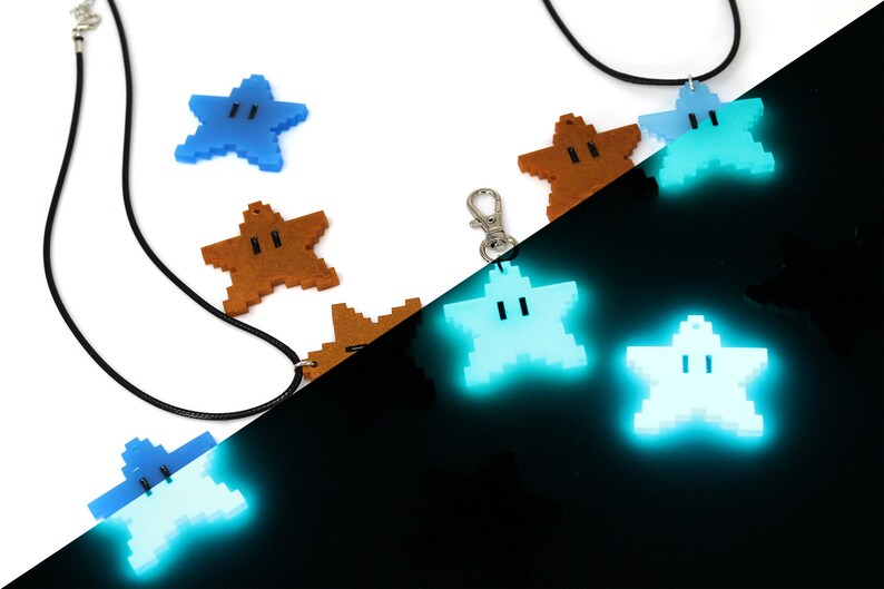 May include: A set of glow-in-the-dark star-shaped pendants with a face on each. The pendants are in different colors, including blue, brown, and light blue. The pendants are on a black cord and a silver chain.