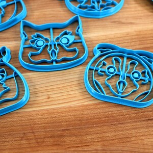 May include: Four blue plastic cookie cutters shaped like owls with different facial expressions. The cutters are on a wooden surface.