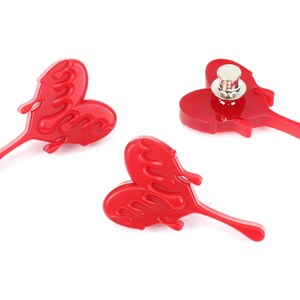 May include: Three red heart-shaped pins with a dripping effect. The pins have a silver metal backing.