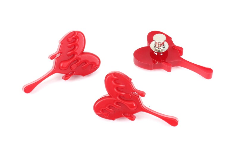 May include: Three red heart-shaped pins with a dripping effect. The pins have a silver metal backing.