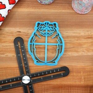 May include: Blue plastic cookie cutter shaped like a cartoon character with large eyes and a round body.