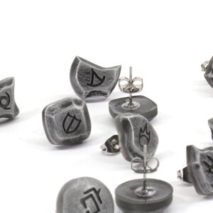 Puede incluir: Un conjunto de pendientes plateados con diferentes s&iacute;mbolos, incluyendo un escudo, una llama, un remolino y una luna creciente. Los pendientes est&aacute;n hechos de metal y tienen un acabado texturizado.