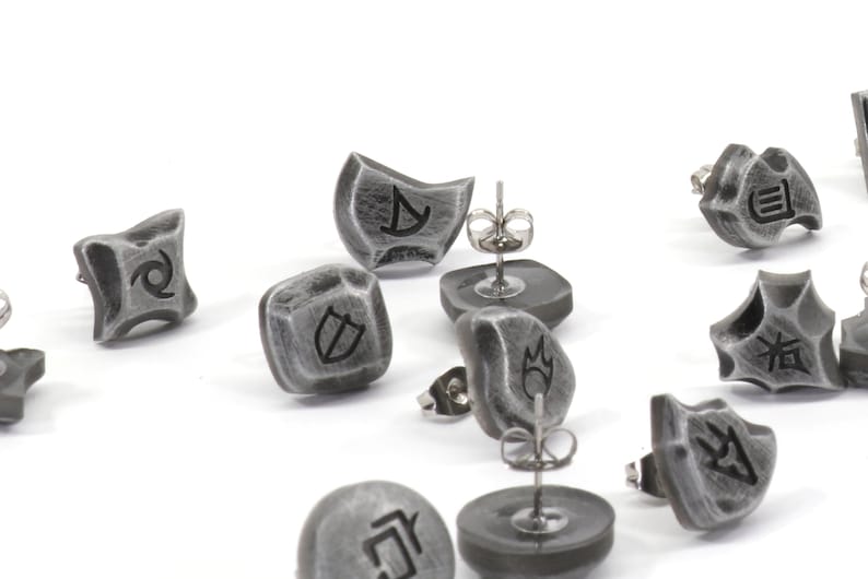 Puede incluir: Un conjunto de pendientes plateados con diferentes s&iacute;mbolos, incluyendo un escudo, una llama, un remolino y una luna creciente. Los pendientes est&aacute;n hechos de metal y tienen un acabado texturizado.