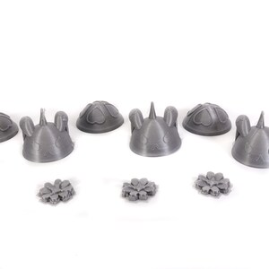 May include: Six gray 3D printed figurines with different designs, including bunny ears, hearts, and a unicorn horn. Three smaller gray 3D printed flower-shaped objects are also included.
