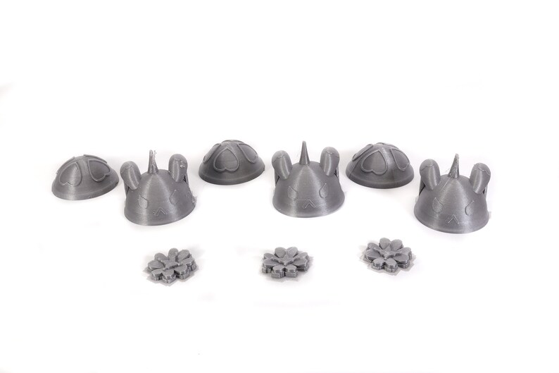 May include: Six gray 3D printed figurines with different designs, including bunny ears, hearts, and a unicorn horn. Three smaller gray 3D printed flower-shaped objects are also included.