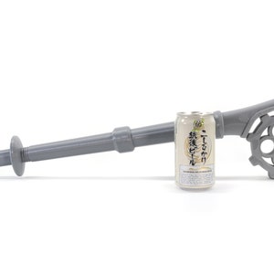 May include: A gray plastic can opener with a long handle and a gear-like mechanism. The opener is designed to open cans of beer. A can of beer is shown next to the opener for scale.