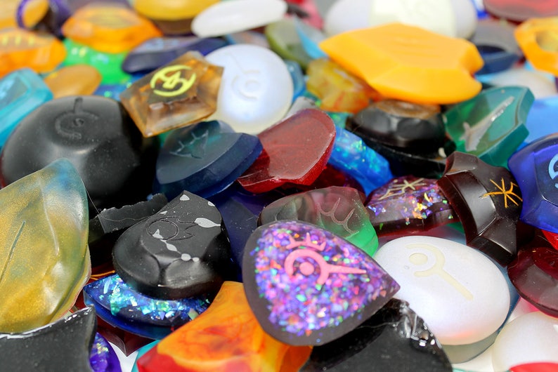 Puede incluir: Una colecci&oacute;n de p&uacute;as de guitarra &uacute;nicas y coloridas con varios dise&ntilde;os y texturas. Algunas p&uacute;as son transparentes, mientras que otras son opacas. Las p&uacute;as est&aacute;n hechas de diferentes materiales, incluyendo pl&aacute;stico, metal y madera.
