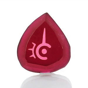Könnte beinhalten: Ein roter, tropfenförmiger Kristall mit einem rosafarbenen Symbol eines stilisierten Auges mit einer Mondsichel und einer Spitze.