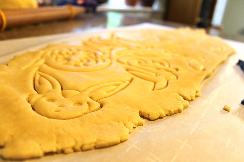 May include: A sheet of unbaked cookie dough with bunny and other shapes cut out. The dough is on a white parchment paper surface.