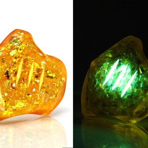 May include: A yellow and gold iridescent resin heart-shaped pendant with three lines carved into it. The pendant glows green under a black light.