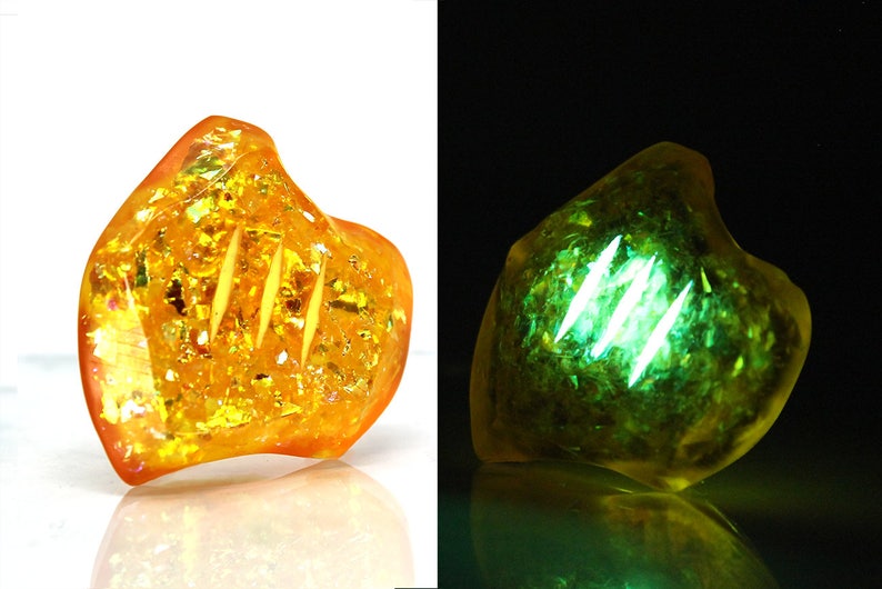 May include: A yellow and gold iridescent resin heart-shaped pendant with three lines carved into it. The pendant glows green under a black light.