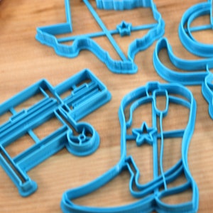 May include: A set of blue plastic cookie cutters shaped like a cowboy boot, a wagon, a longhorn steer, a cowboy hat, and the state of Texas.