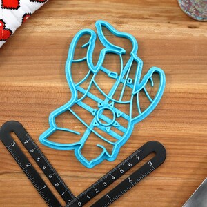 May include: A blue plastic cookie cutter shaped like a hand wearing a striped glove and a sun on the back of the hand.