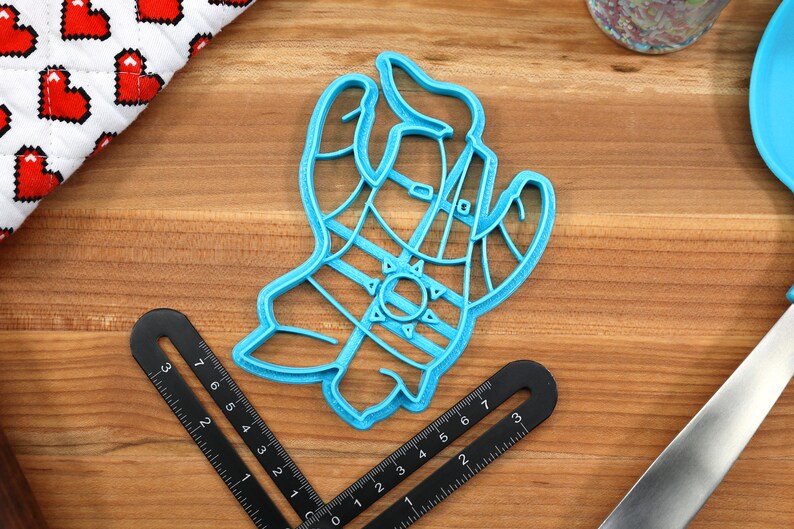 May include: A blue plastic cookie cutter shaped like a hand wearing a striped glove and a sun on the back of the hand.