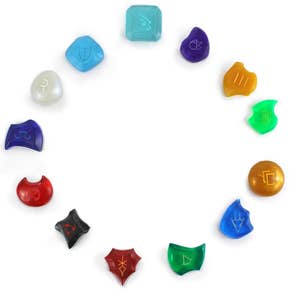 May include: A set of 12 colorful, translucent, gemstone-like dice with different symbols on each face. The dice are arranged in a circle on a white background.