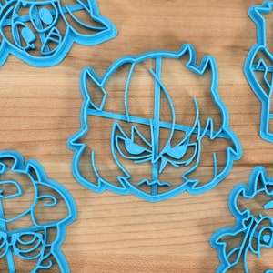 May include: A set of six blue plastic cookie cutters shaped like cartoon characters. The cutters are on a wooden surface.
