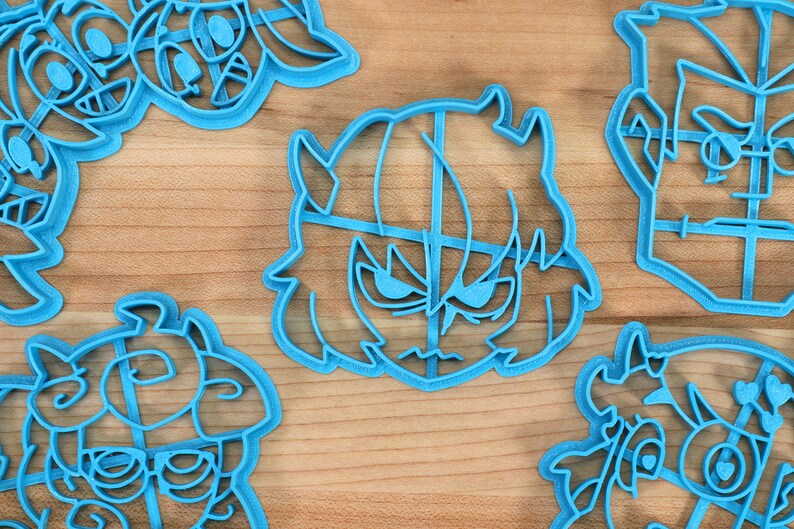 May include: A set of six blue plastic cookie cutters shaped like cartoon characters. The cutters are on a wooden surface.