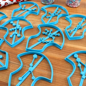 Puede incluir: Ocho cortadores de galletas de pl&aacute;stico azul con forma de camiseta con diferentes dise&ntilde;os de constelaciones.