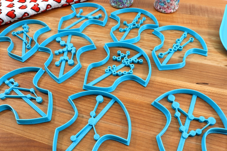 Puede incluir: Ocho cortadores de galletas de pl&aacute;stico azul con forma de camiseta con diferentes dise&ntilde;os de constelaciones.