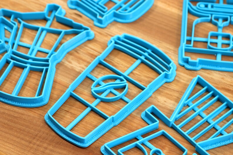 May include: A set of blue plastic cookie cutters shaped like a coffee pot, a coffee cup, a coffee bean, and a coffee shop sign.