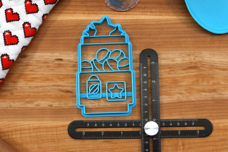 May include: A blue plastic cookie cutter shaped like a gumball machine with a star on top. The gumball machine has a window with gumballs inside and a small star and a bottle with a leaf on the bottom.