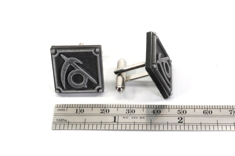 May include: A pair of silver cufflinks with a black and silver design. The design features a stylized symbol with a curved line and a circle.