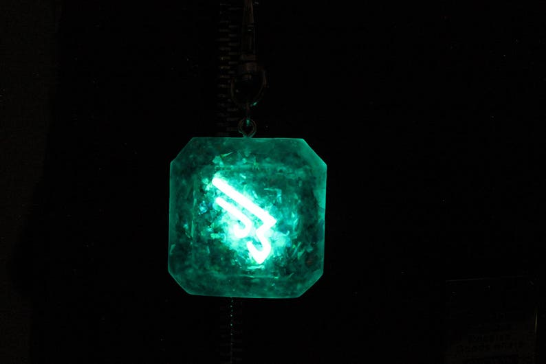 May include: A green, faceted, crystal pendant with a glowing white symbol inside. The pendant is hanging from a chain.