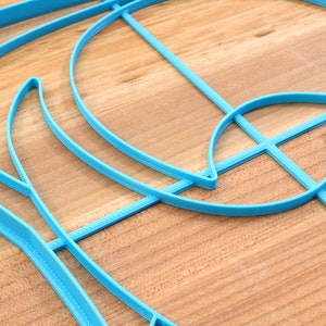 May include: A blue plastic stencil with a geometric design. The stencil is made up of curved lines and shapes.