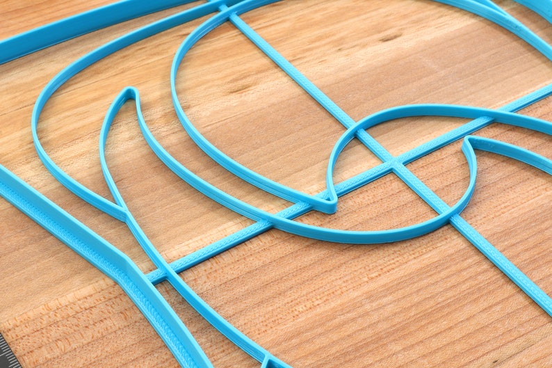 May include: A blue plastic stencil with a geometric design. The stencil is made up of curved lines and shapes.