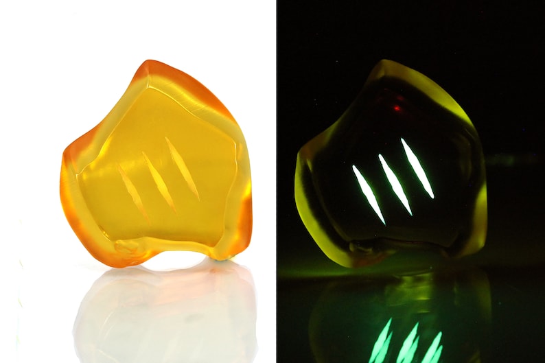 May include: A translucent, amber-colored, abstract sculpture with three diagonal, etched lines. The sculpture glows with a bright green light in a dark setting, creating a striking visual contrast.
